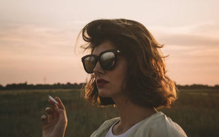 a woman in glasses smoking at dusk